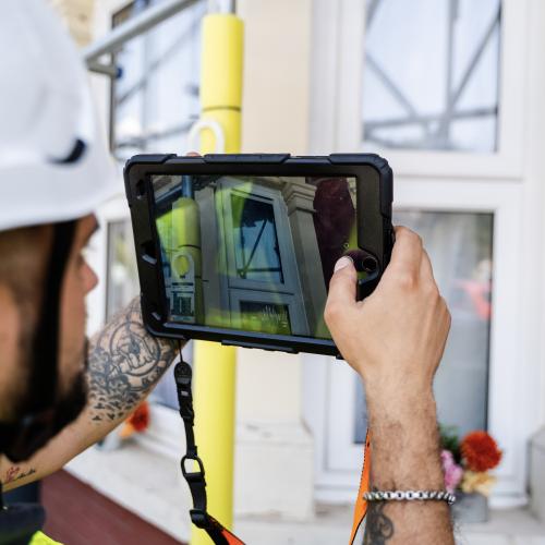 man in hard hat holds inspection device up to building
